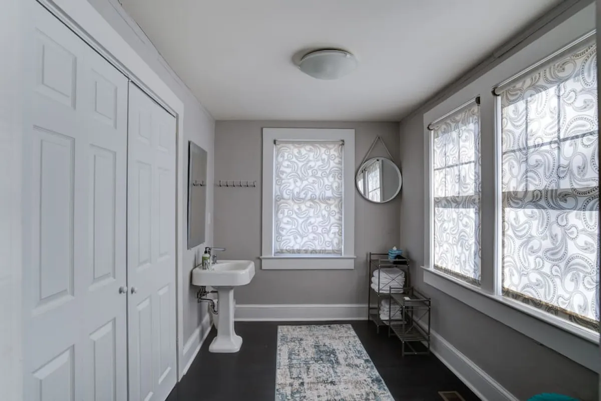 A serene modern bathroom featuring an elegant sink, large mirrors, ample natural light from the windows, and a plush rug. The clean lines and bright, calm mood make the space inviting for daily routines or moments of relaxation.