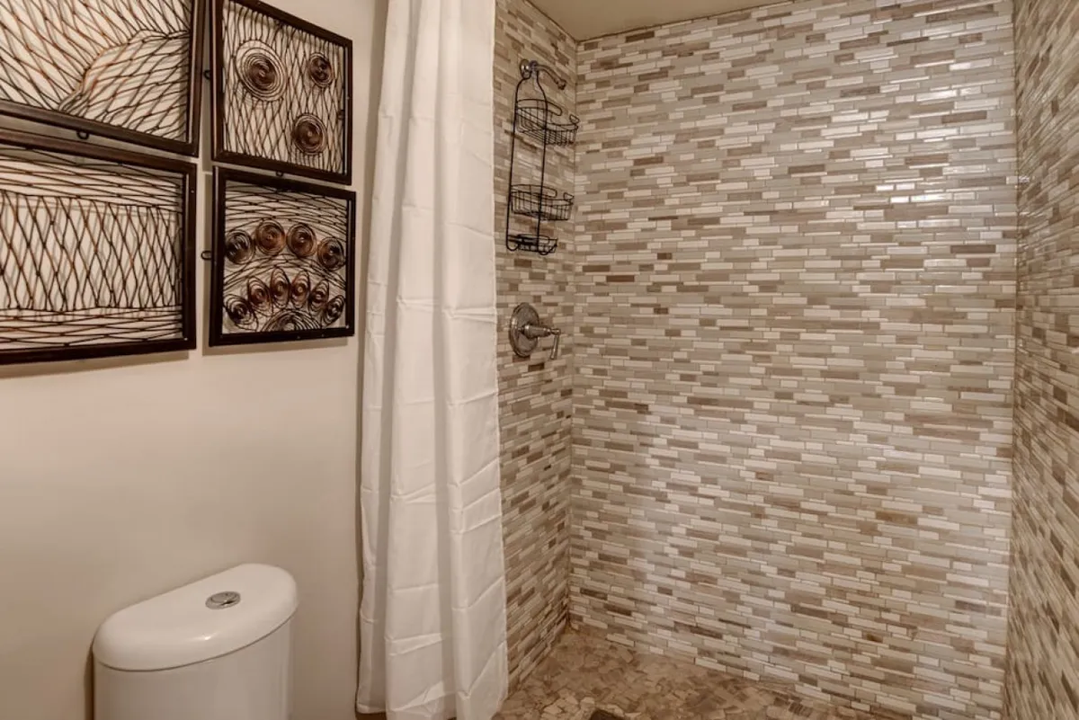 A refined bathroom scene with a striking textured tile wall, modern shower fixtures, framed art, and a neat toilet area. The tranquil mood and attention to design detail evoke a spa-like retreat, highlighting both functionality and sophistication.