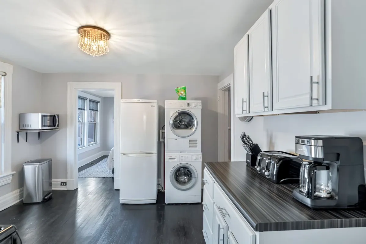 A practical, inviting laundry and kitchen area displaying a washer and dryer, refrigerator, and coffee maker. The scene captures daily life with elements such as folding laundry, brewing coffee, and meal preparation, underlining everyday convenience and comfort.
